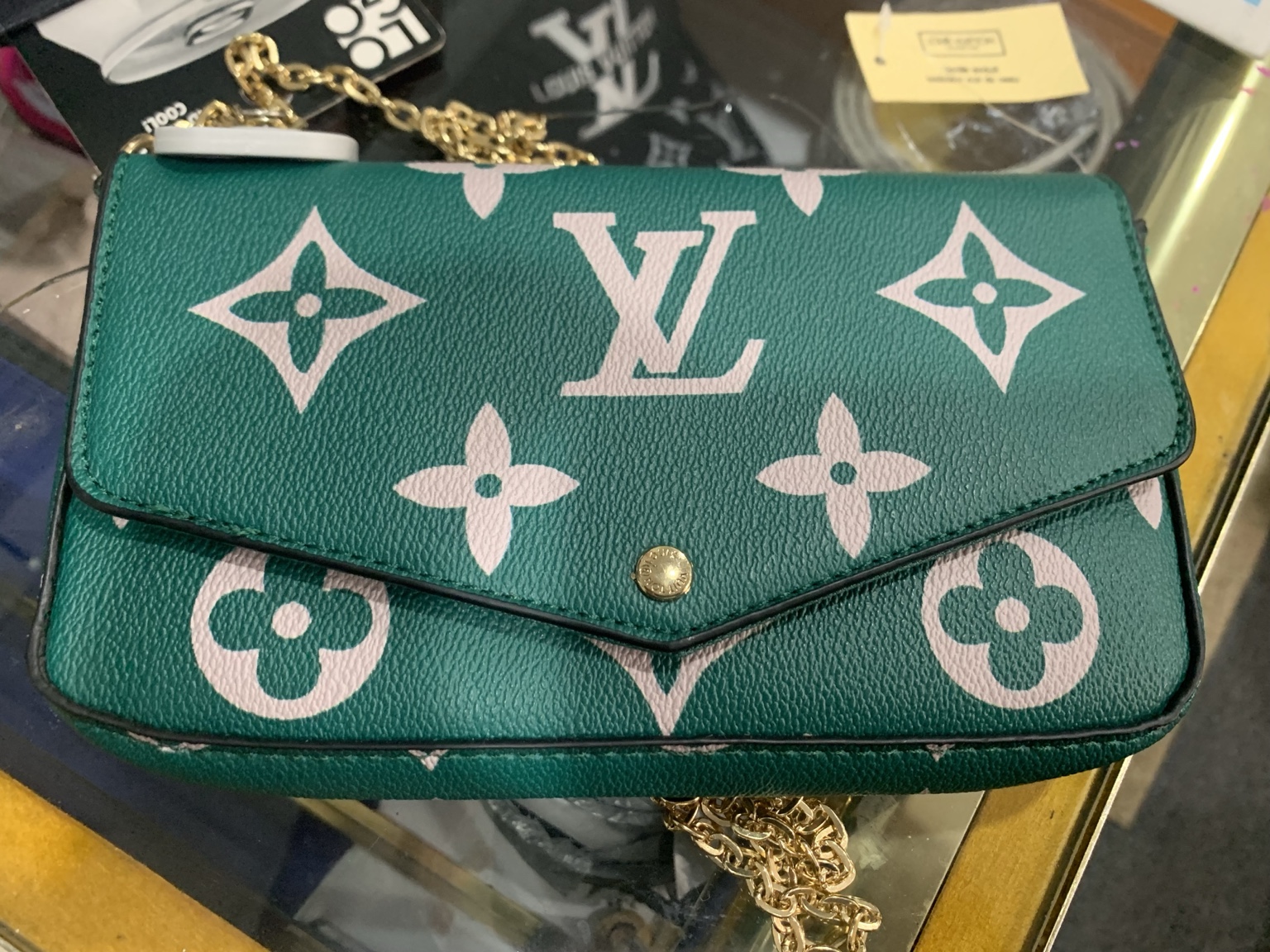 Green envelope-style purse with a pale monogram pattern and a gold-tone chain