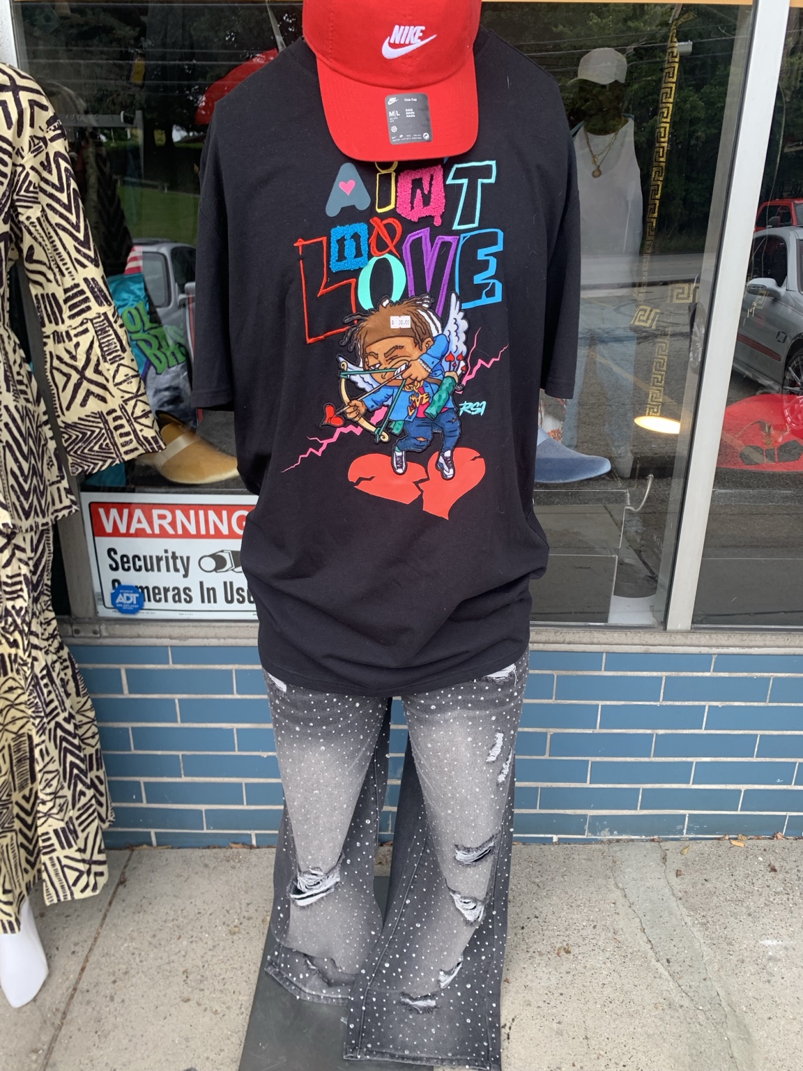 Black colorful graphic tee with gray distressed embellished jeans and a red Nike cap